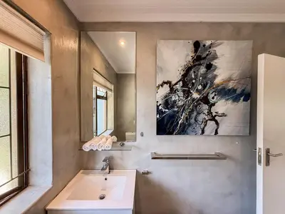 a bathroom with a sink and a painting on the wall at Sandbaai Breeze in Hermanus