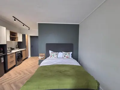 a bedroom with a bed with a green blanket at Trendy Studio Apartment in On Park in Cape Town