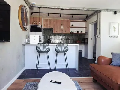 a living room with a kitchen with two bar stools at Green Olive Luxury Stay - Cozy, modern and central in Tygerberg Hills