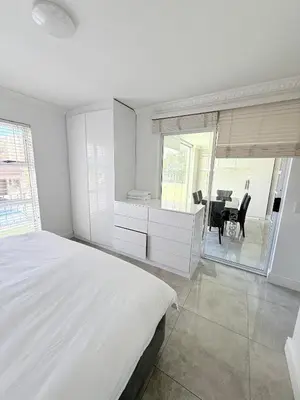 a white bedroom with a bed and a table at Italian luxe 6 sleeper apartment near canal walk in Cape Town