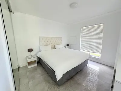 a white bedroom with a large bed and a window at Italian luxe 6 sleeper apartment near canal walk in Cape Town