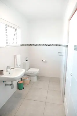 a white bathroom with a toilet and a sink at Abalone at Hermanus Reefs in Hermanus