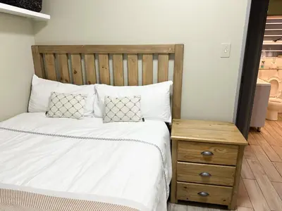 a bed with a wooden headboard and a wooden table at 29 on Windsor Rooms- in Camelot,Kuilsriver in Silver Sands