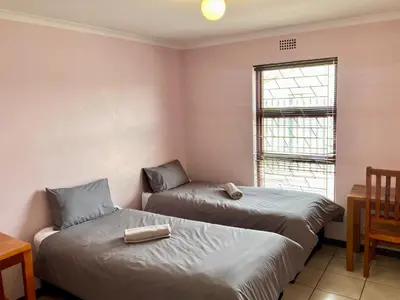 two beds in a room with a table and a window at Unit 1 GatherPoint Sleeps 6 Self-Catering Group in Belhar, Cape Town in Belhar