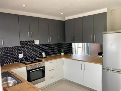 a kitchen with white cabinets and wood counter tops at Unit 1 GatherPoint Sleeps 6 Self-Catering Group in Belhar, Cape Town in Belhar