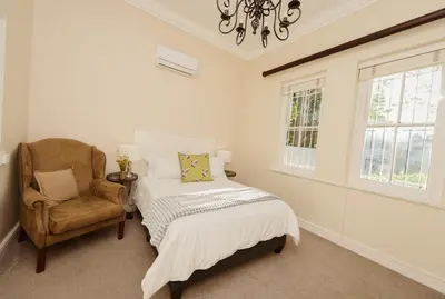 a bedroom with a bed and a chair and a chandelier at Charming Historic Home in Central Stellenbosch in Stellenbosch
