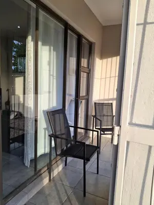 two chairs sitting on a balcony with glass doors at Spacious Suite Somerset West in Somerset West