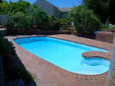 a large swimming pool with a brick pathway around it at Chasselas Studio in Somerset West