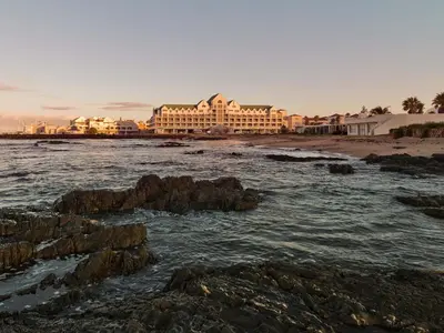 a hotel on the beach with rocks in the water at Krystal Beach Hotel in Gordonʼs Bay