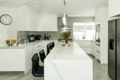 a white kitchen with a long white table and black chairs at Beach House in Sunset Beach in Cape Town