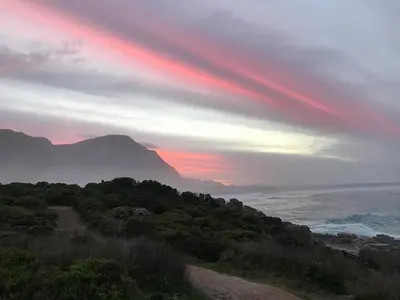 a sunset over the ocean with a mountain at Milkwood Lodge in Hermanus