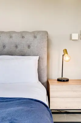 a bedroom with a bed and a lamp on a nightstand at Belina - Knightsbridge Prestige Suite in Cape Town