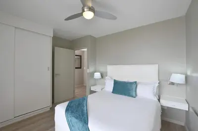 a bedroom with a white bed and a ceiling fan at Luxury Beachside Apartment in Aquarius in Cape Town