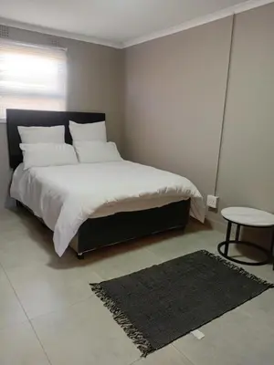 a bedroom with a large bed with white sheets and a table at Home in Brooklyn Cape Town in Cape Town