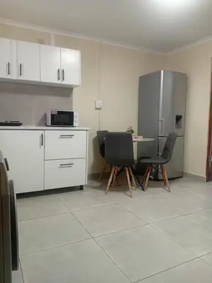 a kitchen with a table and two chairs and a refrigerator at Home in Brooklyn Cape Town in Cape Town