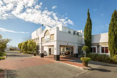 a white building on a street with trees at Protea Hotel by Marriott Stellenbosch & Conference Centre in Stellenbosch