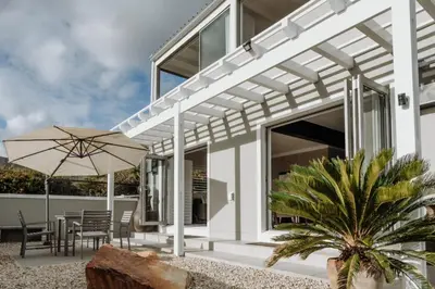 a white house with a patio with a table and an umbrella at Coats Haven in Hermanus