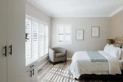 a bedroom with a bed and a chair and windows at Coats Haven in Hermanus