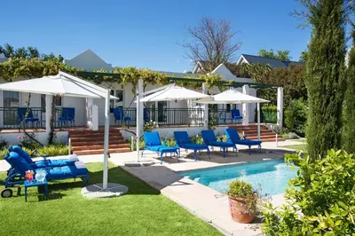 a backyard with a pool with blue chairs and umbrellas at Majeka House Boutique Hotel by The Living Journey Collection in Stellenbosch