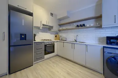 a large kitchen with white cabinets and a dishwasher at Nua Chic Stylish 1Bedroom - 2mins to Beach in Cape Town