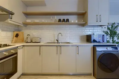 a kitchen with white cabinets and a sink and a dishwasher at Nua Chic Stylish 1Bedroom - 2mins to Beach in Cape Town