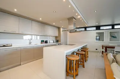 a kitchen with white cabinets and a bar with stools at Harbour House Hotel in Hermanus