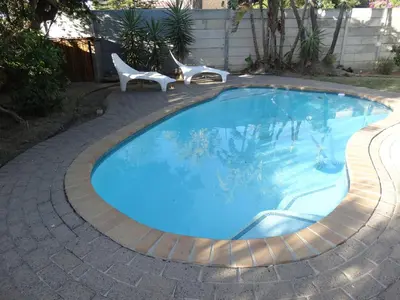 a swimming pool with two white chairs next to it at African Oasis Morrocco in Somerset West