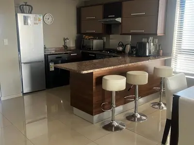 a kitchen with a counter and a refrigerator and stools at Aquarius Luxury Suites 406 in Cape Town