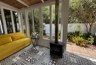 a screened in porch with a yellow couch and a wood stove at Elevené - one bedroom cottage with private pool in Franschhoek