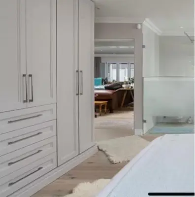 a white kitchen with white cabinets and a living room at Sues Suite in Somerset West