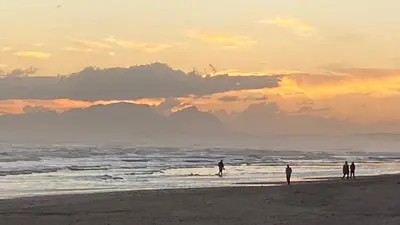 a group of people standing on the beach at sunset at Sea Breeze in Strand