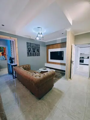 a living room with a brown couch and a television at Beachwalk luxury one bedroom apartments in Cape Town
