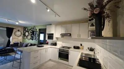 a kitchen with white cabinets and a living room at Her Sanctuary in Cape Town