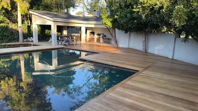 a swimming pool with a wooden deck and a house at Large and spacious family home is leafy suburb in Stellenbosch
