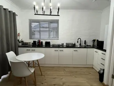 a kitchen with white cabinets and a white table at Layover on Loerie in Cape Town