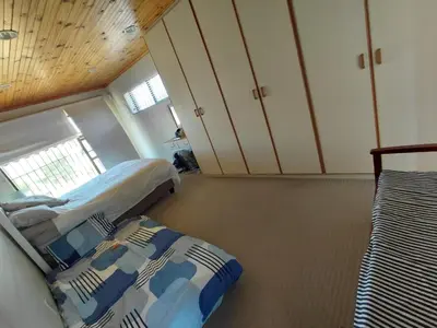 a bedroom with two beds in a room with wooden ceilings at HuisieBydieC in Hermanus