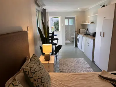 a bedroom with a bed and a kitchen with a table at Secluded Silver Mile with solar back-up in Cape Town