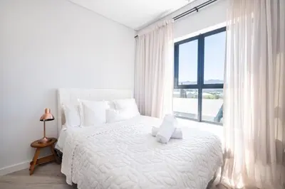 a white bedroom with a white bed and a large window at 232 Paarl Studio With AC and Onsite Parking in Paarl