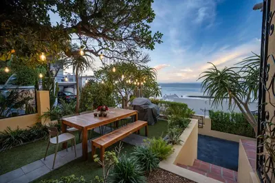 a patio with a wooden table and chairs and the ocean at Villa Solara, 6 bedroom Vacation Villa with sea view in Gordonʼs Bay