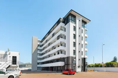 a white building with a red car parked in a parking lot at Burmeister Modern 2-Bedroom w/ Views Milnerton in Cape Town