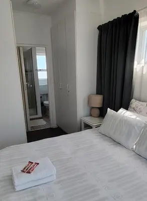 a bedroom with a large white bed with a mirror at Windy Corner Luxury Apartment in Gordonʼs Bay