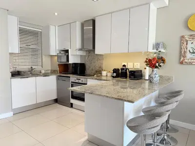 a kitchen with white cabinets and a counter with stools at Instellies Self Catering Apartment in Stellenbosch