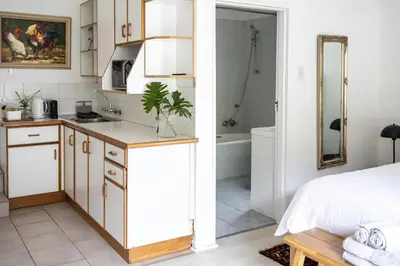 a kitchen with white cabinets and a bathroom with a bed at Private Garden Flat in Die Boord with Secure Parking in Stellenbosch