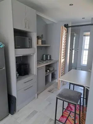 a kitchen with white cabinets and a table with chairs at The Pink Flamingo Self Catering Accommodation in Cape Town