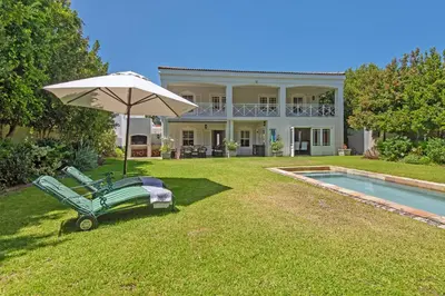 a large house with an umbrella and a pool at Fir Close 3 bedroom in Hermanus