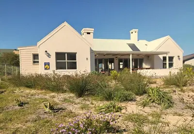 a house on the beach with flowers in the foreground at Taylah's Hideaway in Bettyʼs Bay
