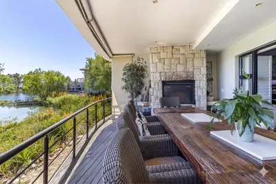 a deck with a wooden table and chairs and a fireplace at Luxury Lakeside Lodge at Jack Nicklaus Golf Estate in Simondium