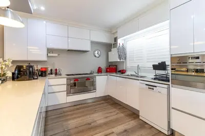 a white kitchen with white cabinets and wooden floors at Luxury Lakeside Lodge at Jack Nicklaus Golf Estate in Simondium