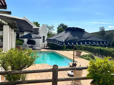 a swimming pool with an umbrella next to a house at Monkscowl Estate in Stellenbosch