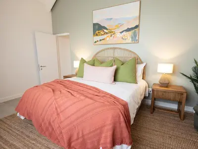 a bedroom with a bed with green and pink pillows at Cornercade | Unit 1 in Hermanus